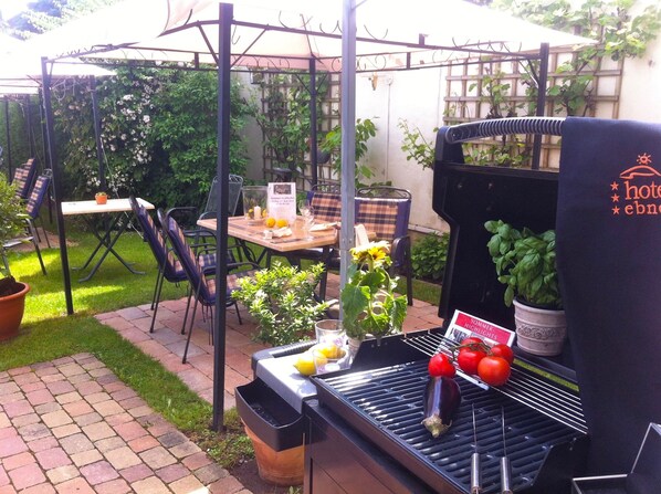 Un patio al aire libre con una parrilla, zona de estar y una pérgola.