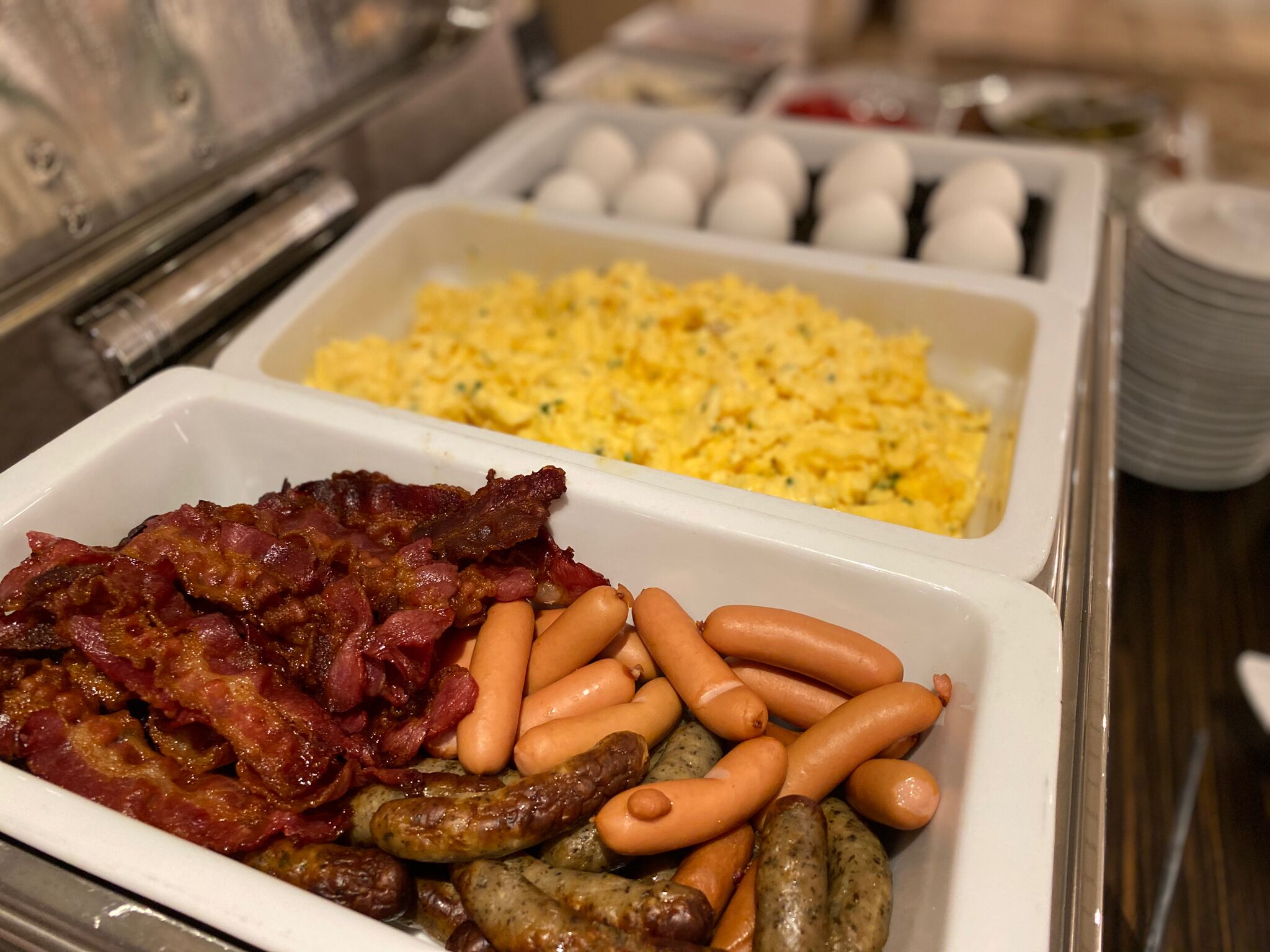A buffet with various food options including bacon, sausages, and scrambled eggs.