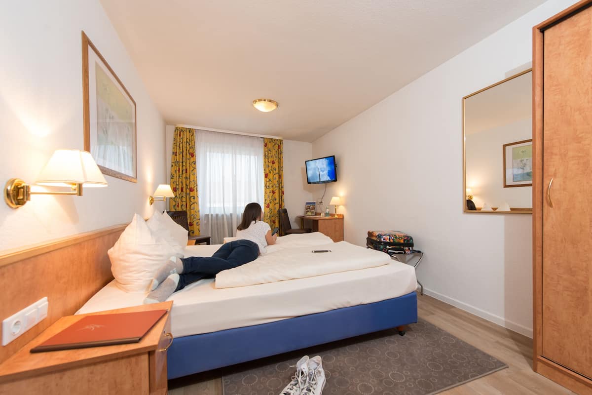 A hotel room with a bed, a television, a desk with a lamp, and a wardrobe.