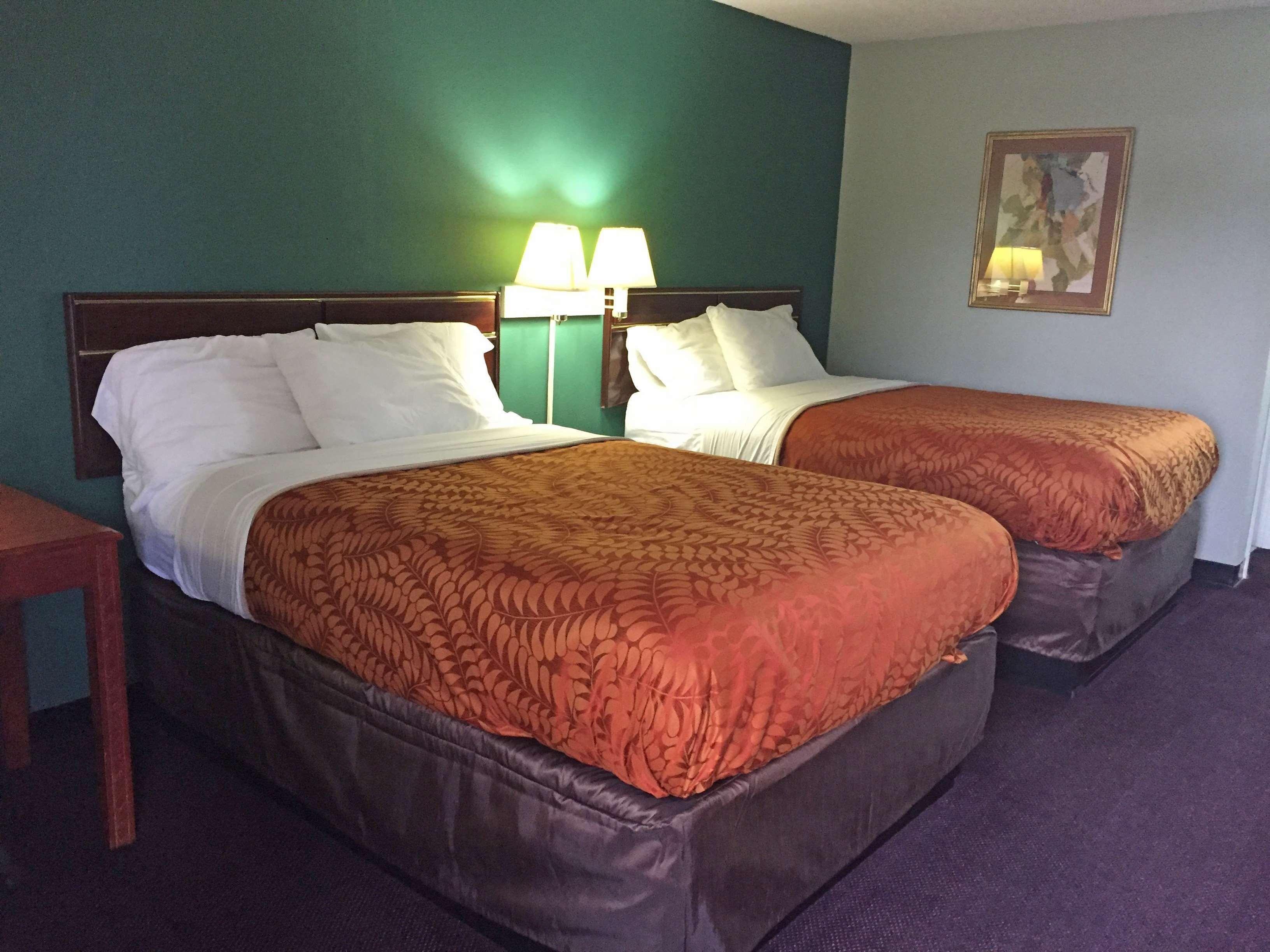Une chambre d’hôtel avec deux lits, une table de chevet, une lampe et un tableau au mur.