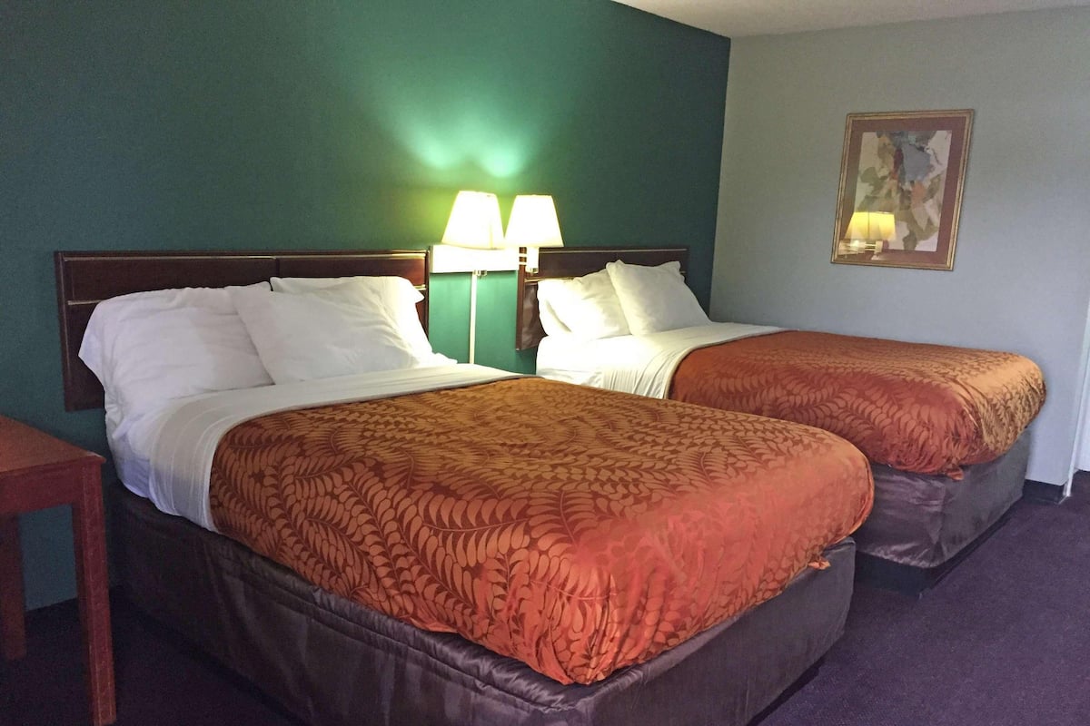 A hotel room with two beds, a nightstand, a lamp, and a painting on the wall.