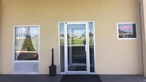 A building entrance with a sliding glass door, a small window with a curtain, and a neon 'OPEN' sign. - Americas Best Value Inn Manchester, TN (Manchester)