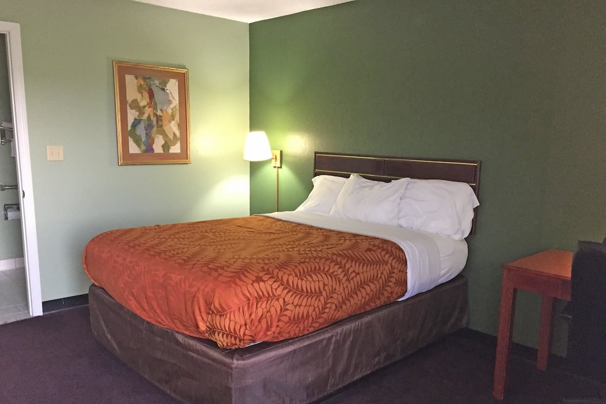 A hotel room with a bed, a nightstand, a lamp, and a painting on the wall.