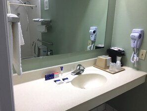 Bathroom features a large mirror above a sink with toiletries and a hairdryer.