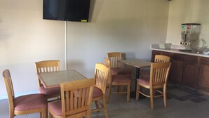 A dining area with wooden tables and chairs, a flat-screen TV mounted on the wall, and a kitchen counter with a coffee machine. - Americas Best Value Inn Manchester, TN (Manchester)