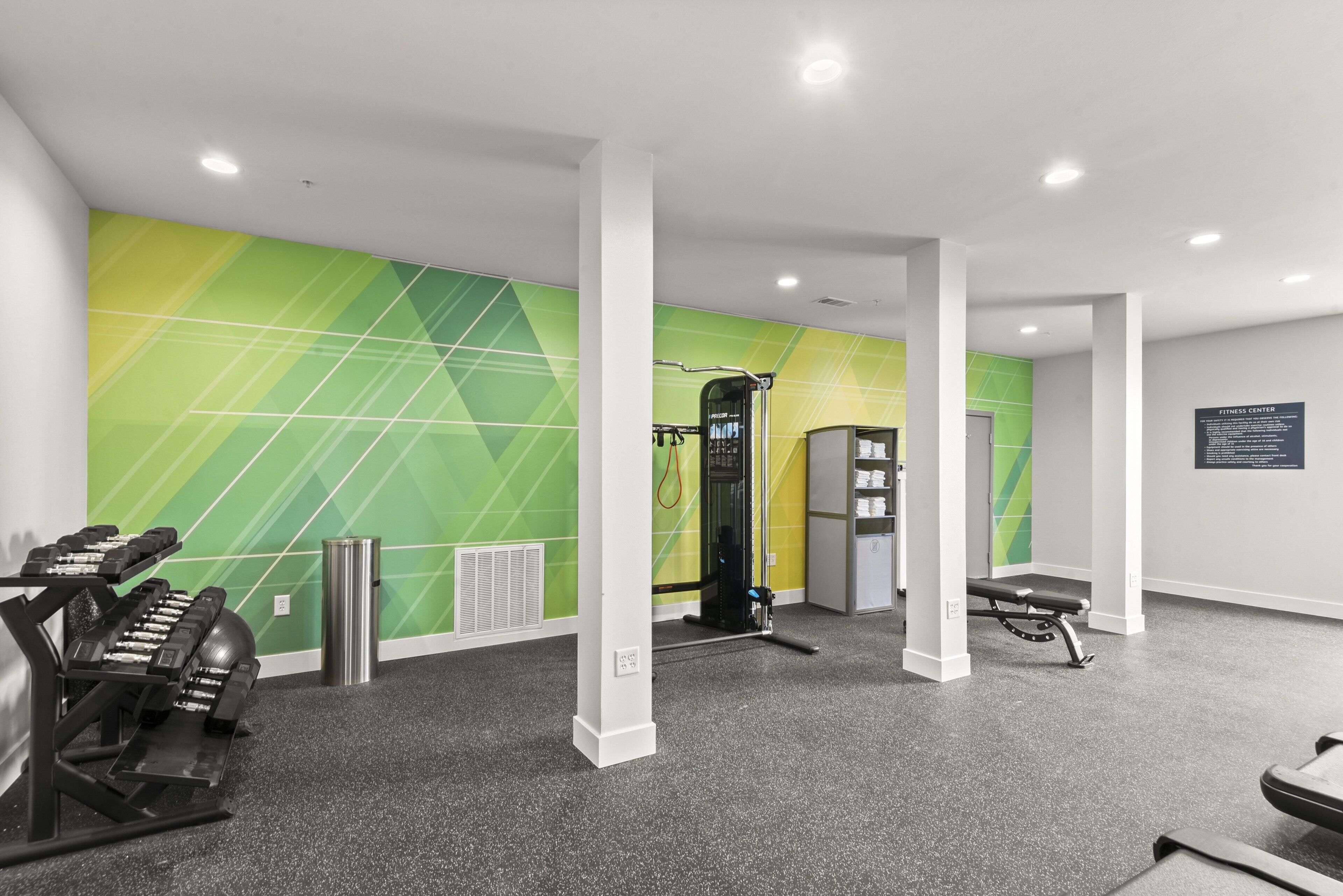 Un centre de remise en forme équipé de matériel d’exercice, un mur orné de motifs géométriques et un banc.