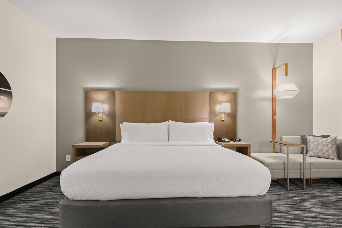 A hotel room with a large bed, two bedside tables, a nightstand, a lamp, and a sofa.
