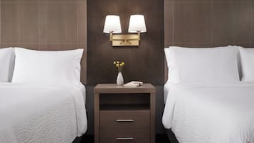 Habitación de hotel con dos camas, una mesita de noche con dos lámparas fijadas a la pared, un florero con flores amarillas y un libro.