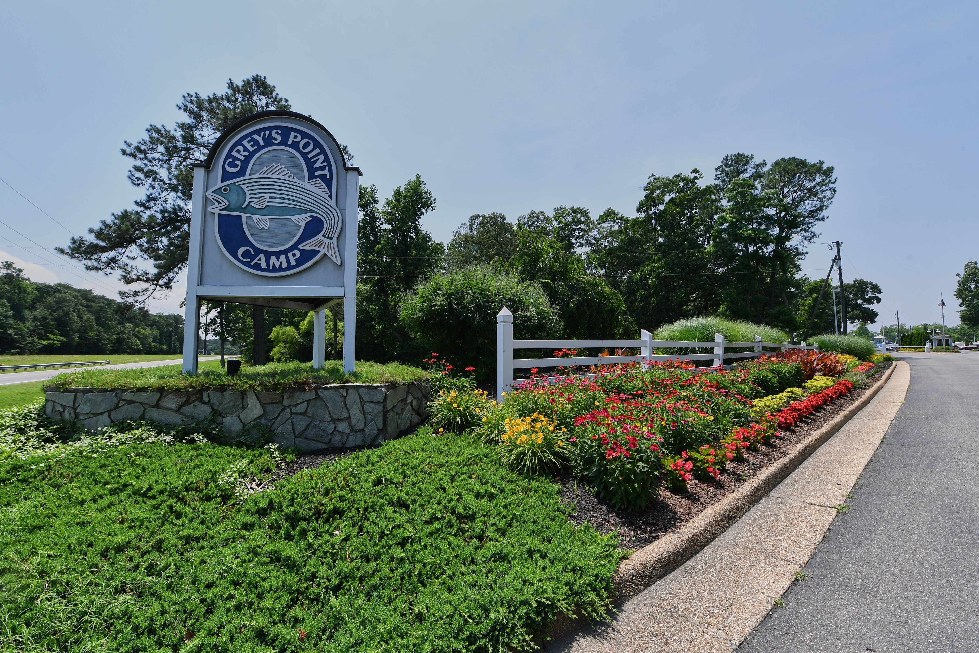 A sign for Grey's Point Camp with a stone wall and flower beds.