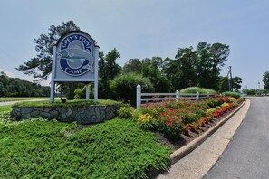A sign for Grey's Point Camp with a stone wall and flower beds.