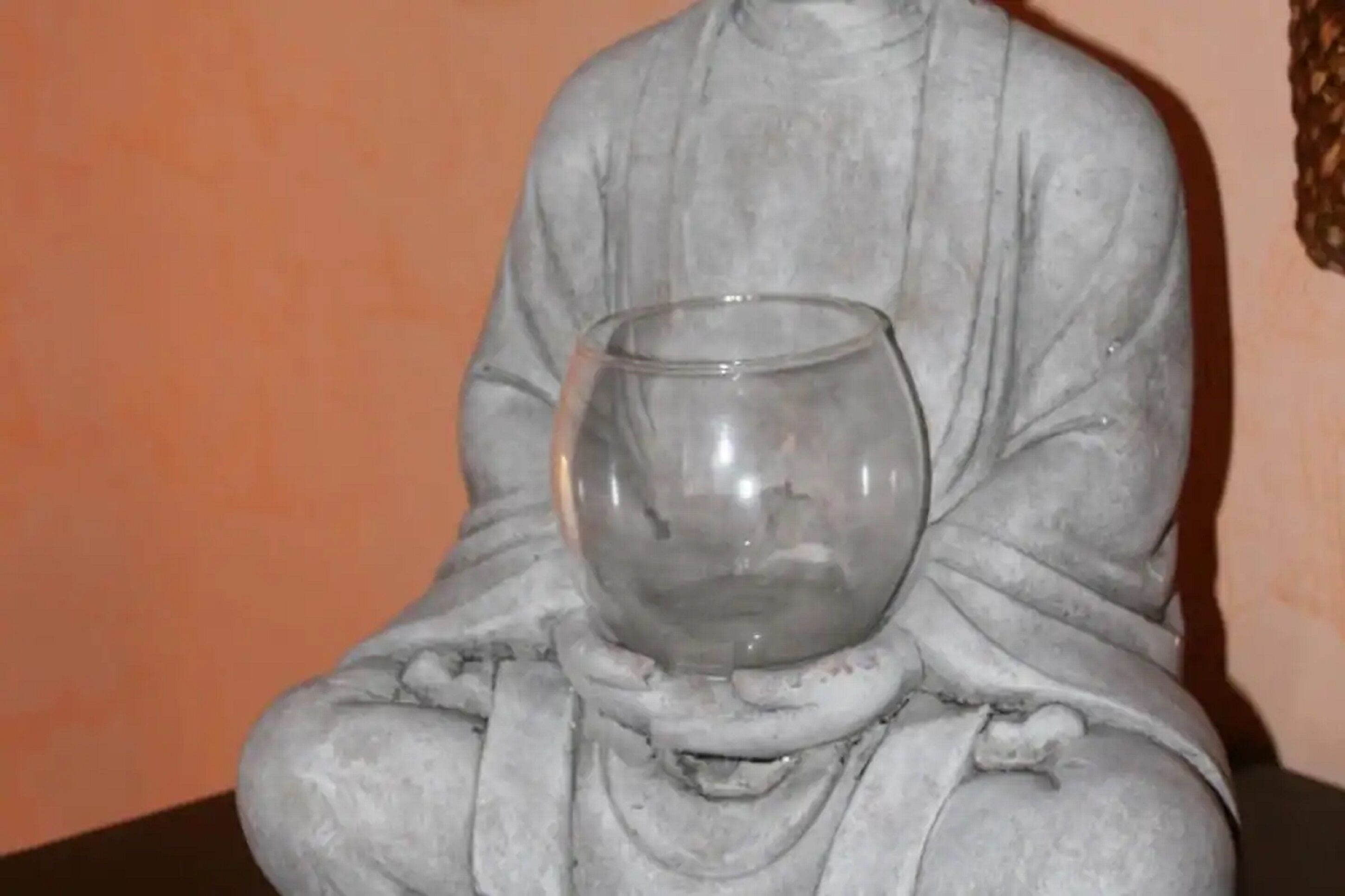 A statue of a seated figure holding a clear glass bowl.