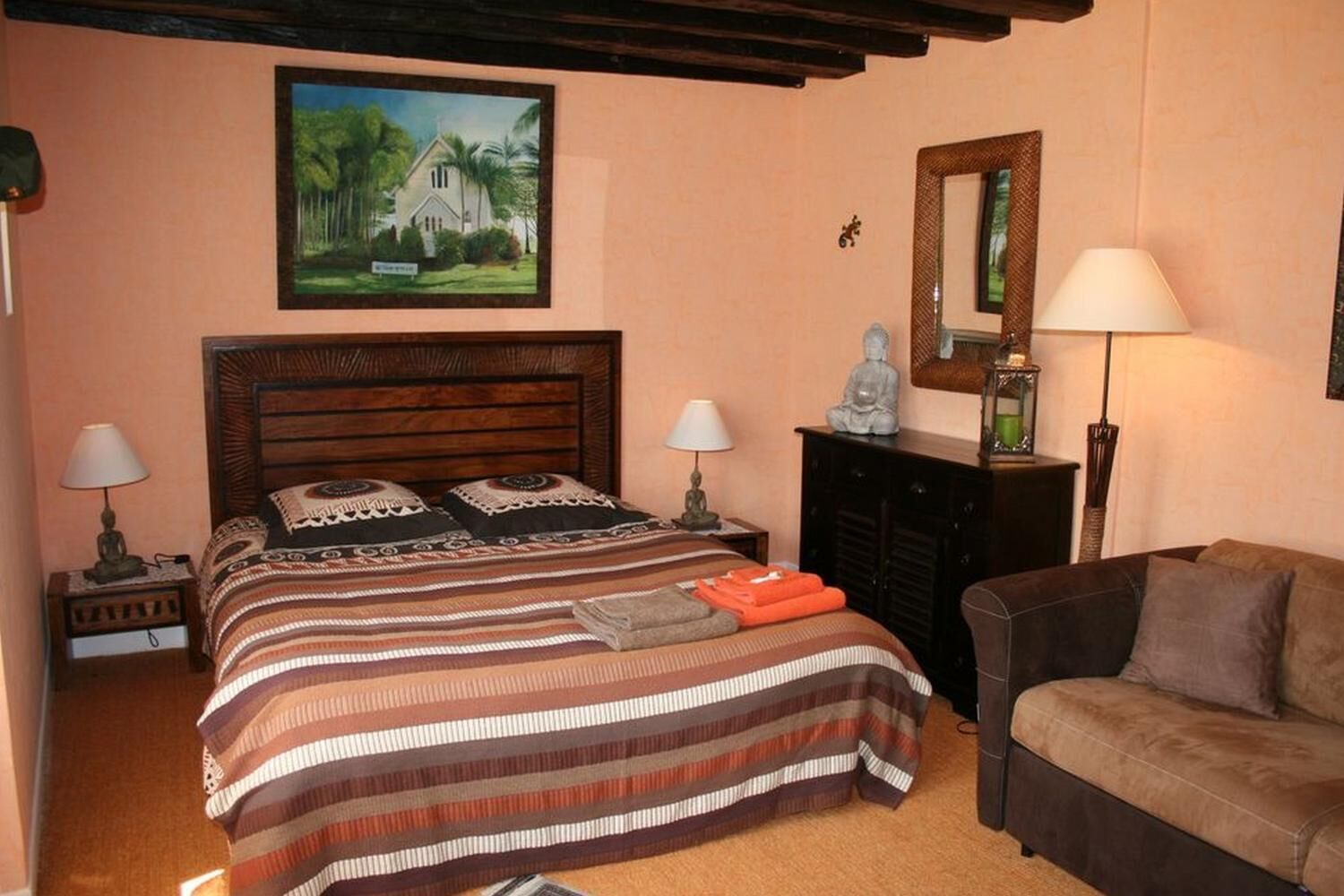 Une chambre à coucher avec un lit en bois, deux tables de chevet avec des lampes, un canapé, une cheminée et un tableau au mur.