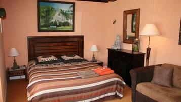 Un dormitorio con cama de madera, dos mesitas de noche con lámparas, un sofá, una chimenea y un cuadro en la pared.