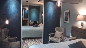 A hotel room with a large bed, two armchairs, a desk, and a chair. There is a ceiling fan and a lamp on the desk. - Le Petit Nailly (Magny-les-Hameaux)