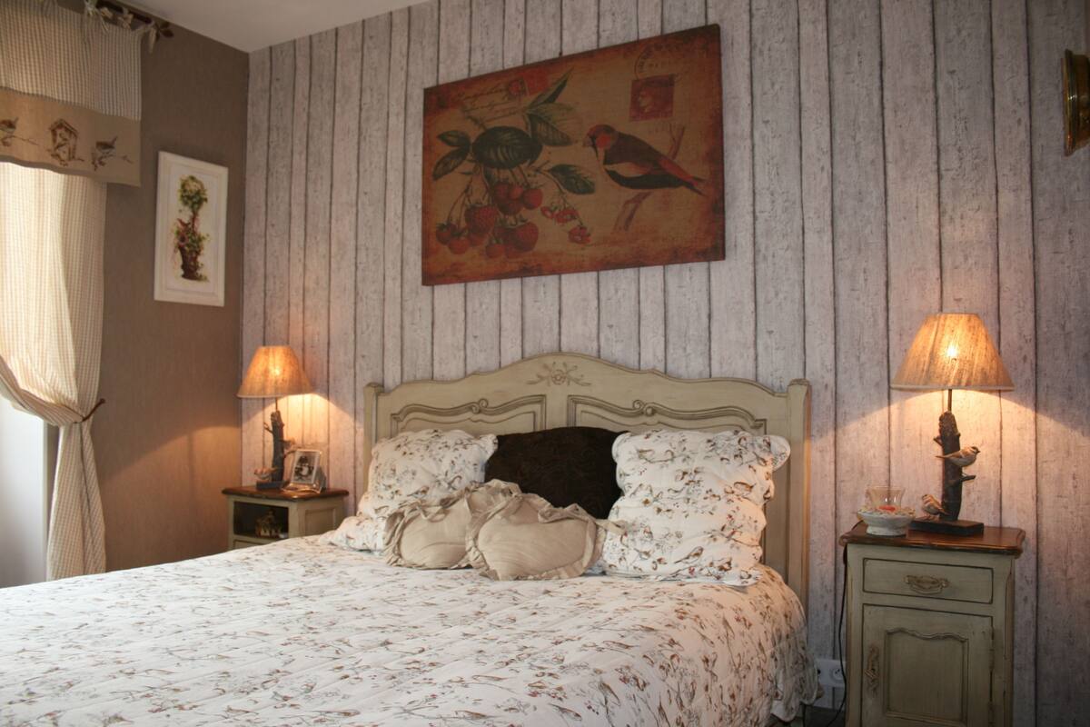 Een slaapkamer met een bed, twee nachtkastjes, een wanddecoratie en een raam met gordijnen.