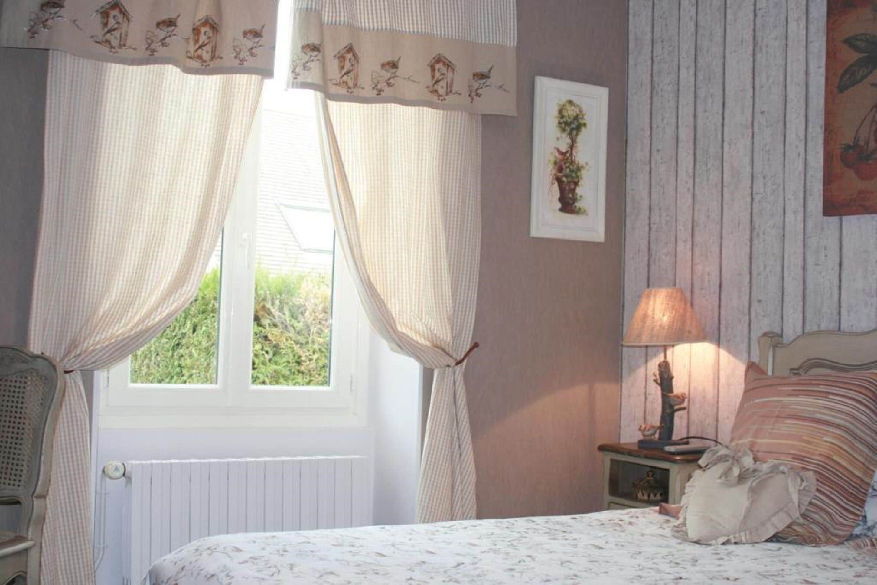 A bedroom with a bed, a nightstand with a lamp, a chair, and curtains.