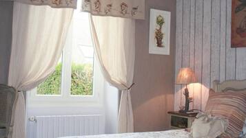 A bedroom with a bed, a nightstand with a lamp, a chair, and curtains.