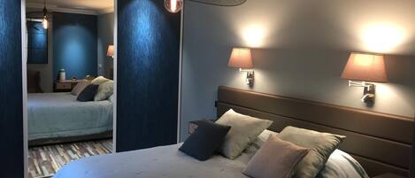 A hotel room with a large bed, two bedside lamps, a hanging light fixture, and a mirror.