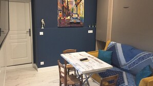 A dining area with a table and chairs, a sofa, and a painting on the wall. - Le Petit Nailly (Magny-les-Hameaux)