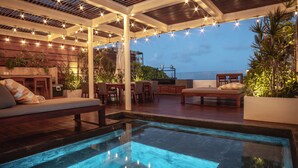An outdoor pool area with a wooden deck, lounge chairs, and string lights. - Downtown Villa (Playa del Carmen)