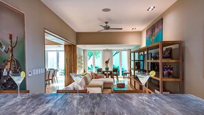 A spacious living area with a large sofa, a dining table, and a bookshelf. There is a ceiling fan and a large window providing natural light. - Downtown Villa (Playa del Carmen)