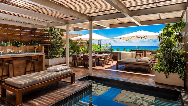 A poolside area with a wooden deck, lounge chairs, a bar, and umbrellas overlooking the ocean. - Downtown Villa (Playa del Carmen)