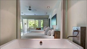 A modern bathroom with a large white bathtub, a ceiling fan, recessed lighting, and a view of a balcony with a table and chairs. - Downtown Villa (Playa del Carmen)