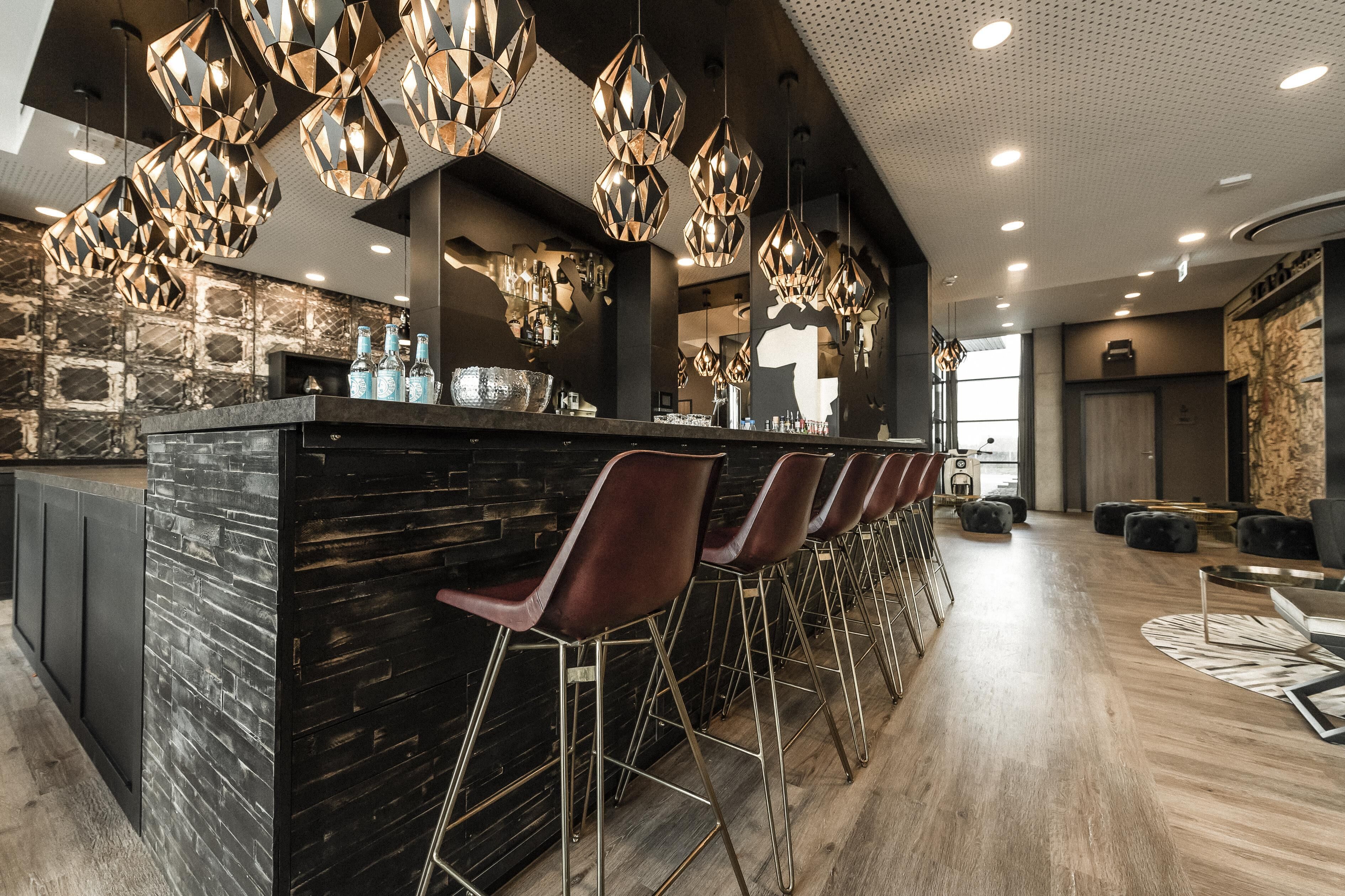 Een moderne bar met een centraal eiland, barstoelen en hanglampen.