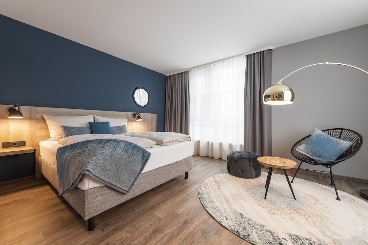 A modern bedroom with a bed, bedside table, lamp, chair, and a round rug.