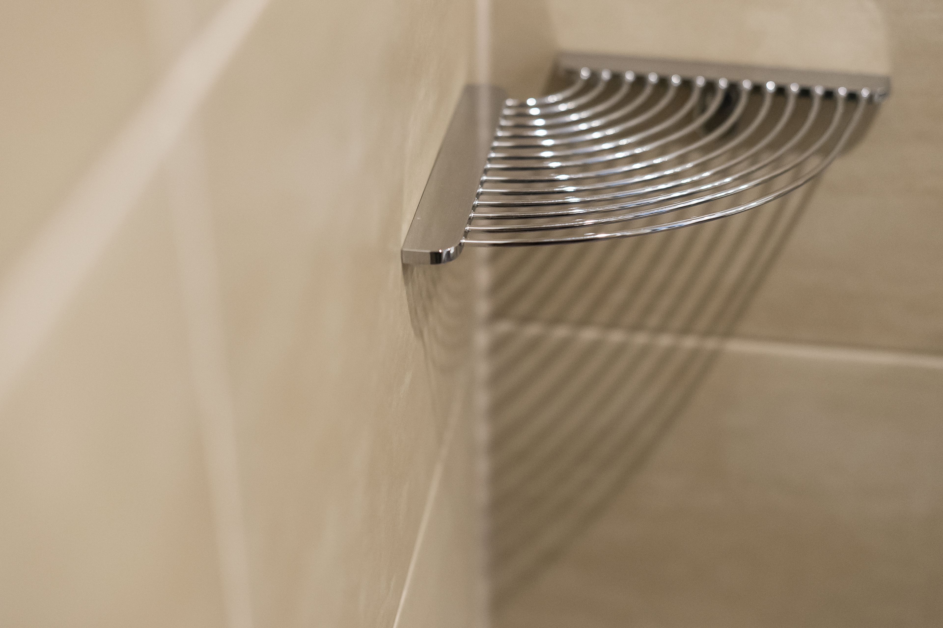 A metallic towel rack with a curved design, mounted on a beige tiled wall.
