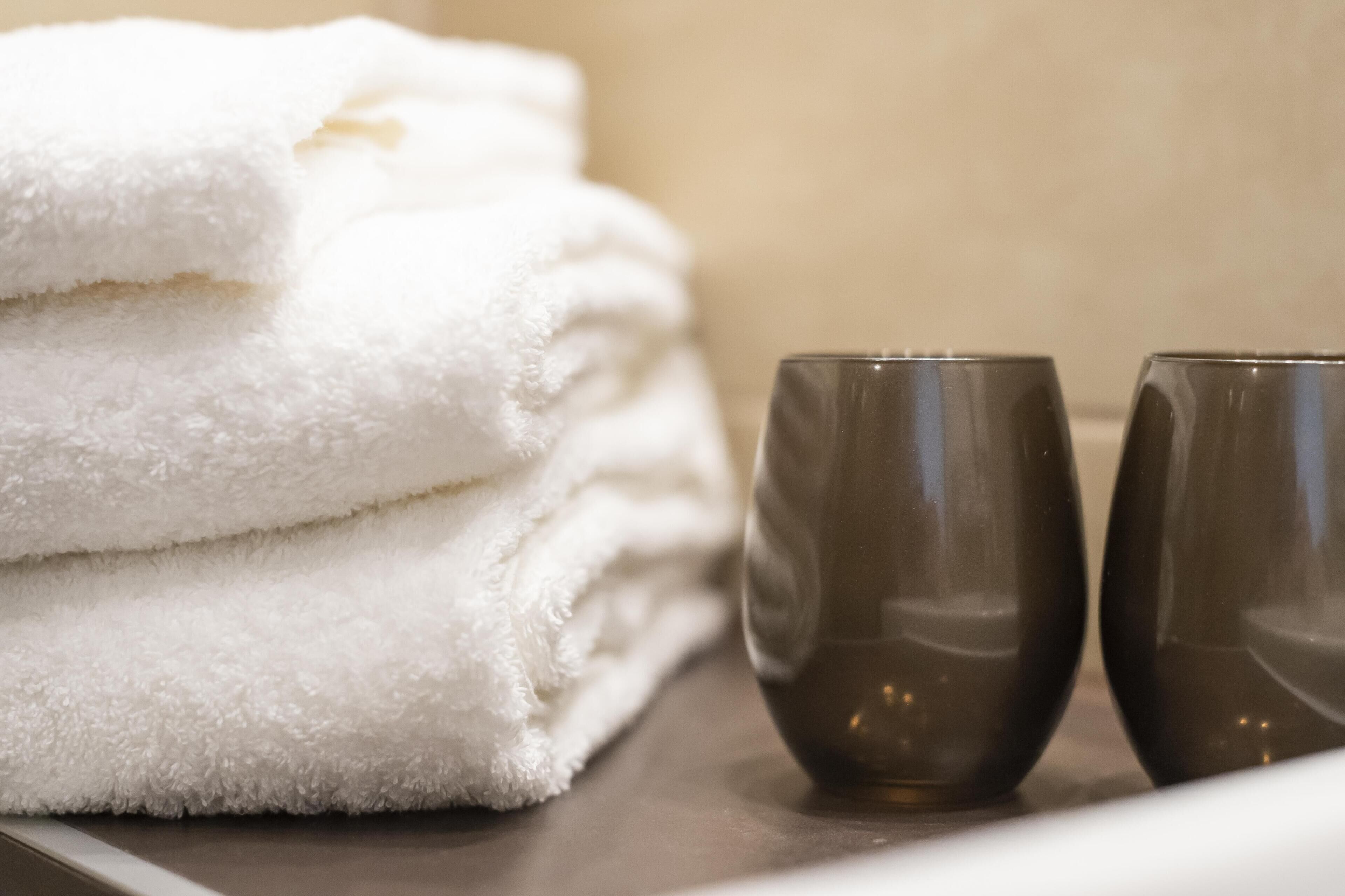 A stack of white towels and two dark glasses on a surface.