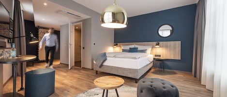 Una habitación de hotel moderna con cama, mesita de noche, lámpara y un espejo redondo en la pared.