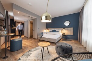 Una habitación de hotel moderna con cama, mesita de noche, lámpara y un espejo redondo en la pared.