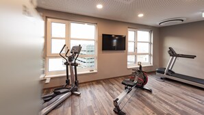 A gym with treadmills, an elliptical, and a stationary bike. There are large windows with a view of buildings outside. - HARBR. Hotel Heilbronn, a member of Radisson Individuals (Heilbronn)