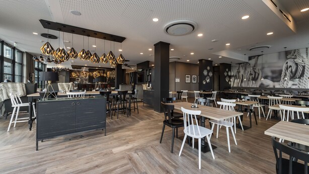 Ein modernes Restaurant mit Holzboden, schwarzen und weißen Stühlen und Pendelleuchten.