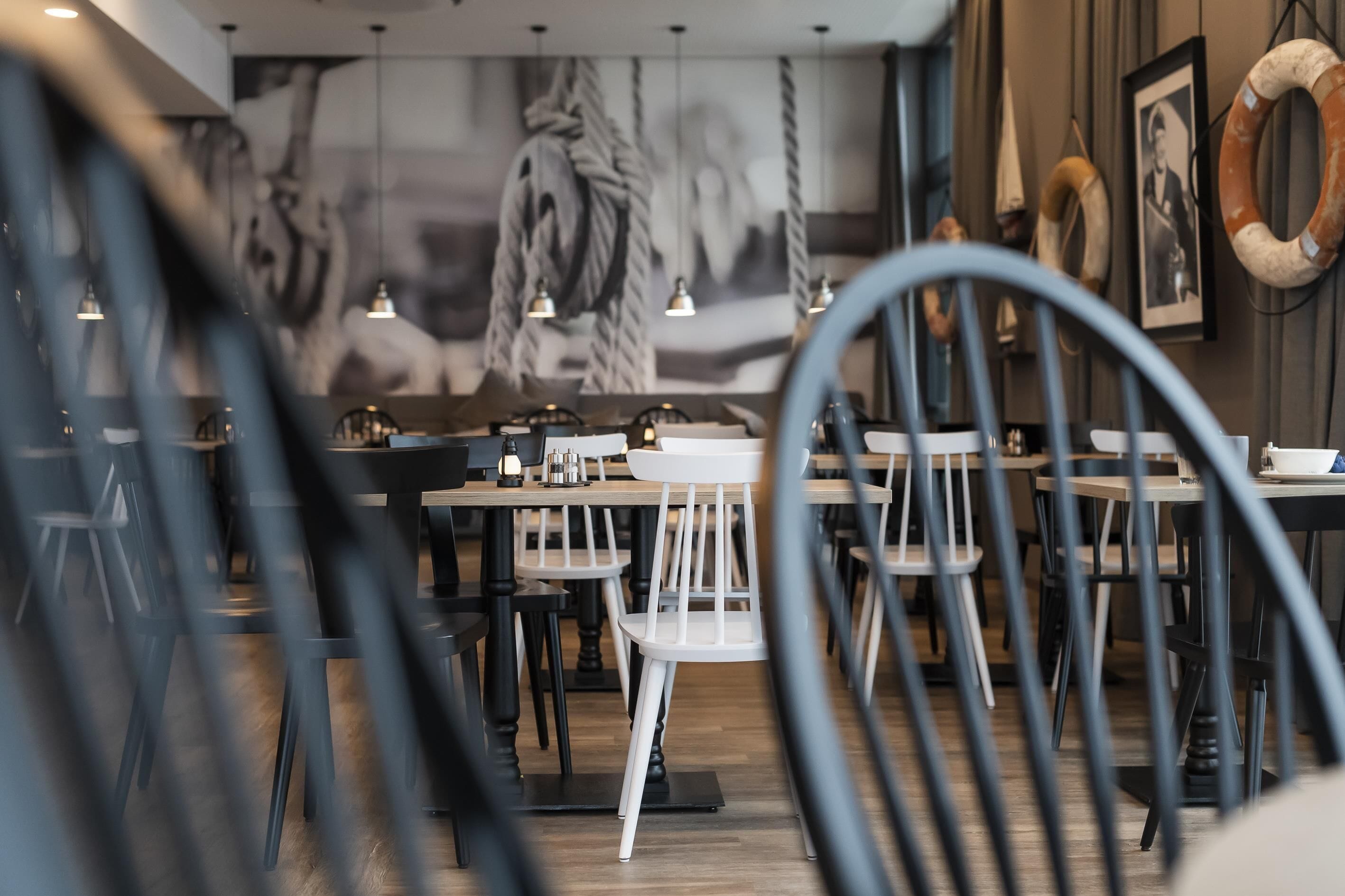 A restaurant interior with multiple tables and chairs, pendant lighting, and a mural on the wall.