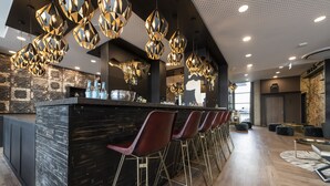 Eine moderne Bar mit schwarzem Tresen, roten Barhocker und geometrischer Pendelleuchte.