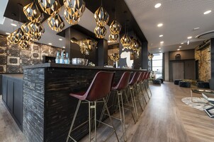 Zona de bar moderna con mostrador negro, taburetes rojos e iluminación colgante de estilo geométrico.