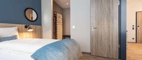 Una habitación de hotel moderna con una cama grande, un armario de madera y un espejo en la pared.