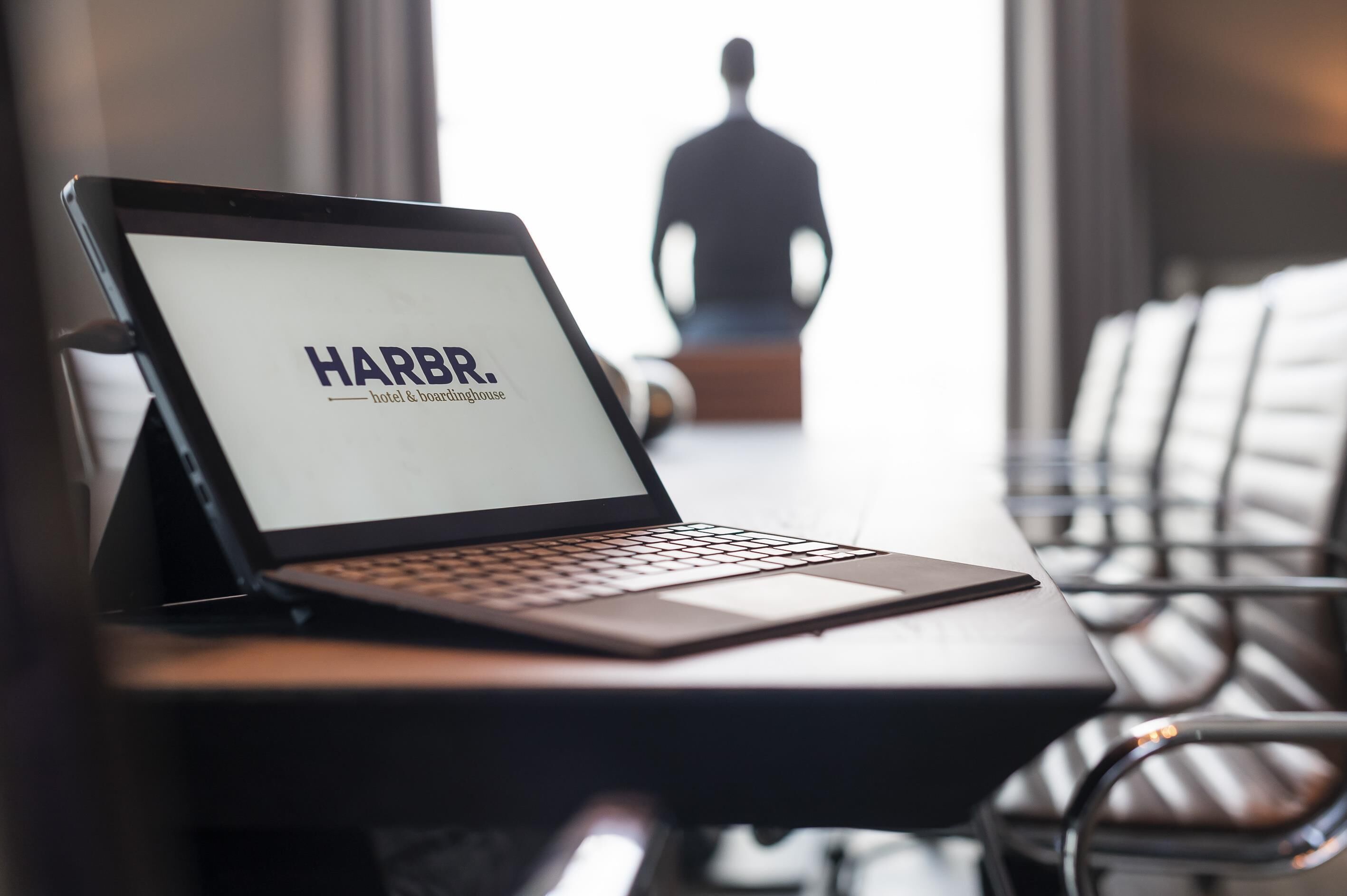 Un ordinateur portable est posé sur un bureau, et son écran affiche le texte « HARBR. hôtel et maison de tourisme ».
