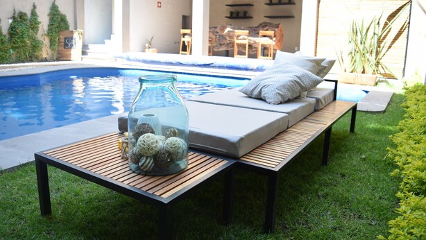 Un área junto a la piscina con una silla de descanso, un tarro de vidrio con adornos y una mesa de madera.