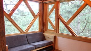 Un banco de madera con asiento y respaldo acolchados, ubicado frente a una pared con amplias ventanas.