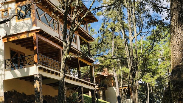 Un edificio de varios pisos con balcones y cimientos de piedra, rodeado de árboles y un área verde.