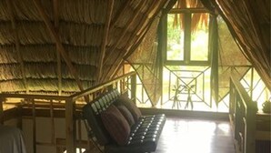Una habitación con techo de paja, una banca de madera y vistas al verdor exterior.