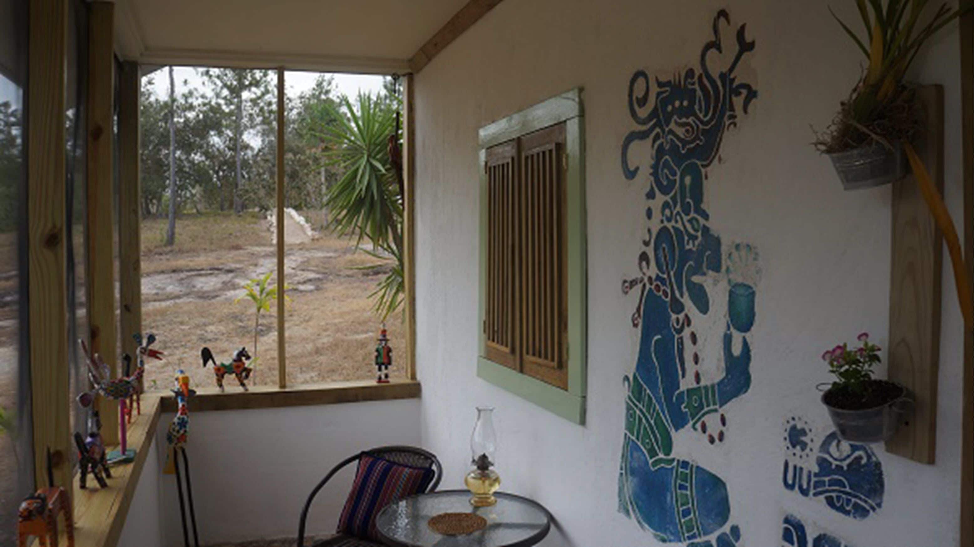 A room with a large window, a table with a glass vase, and a wall with a mural.