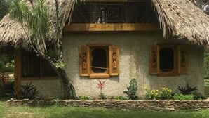 Una casa con techo de paja y balcón, rodeada de vegetación.