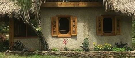A thatched-roof house with a balcony, surrounded by greenery.