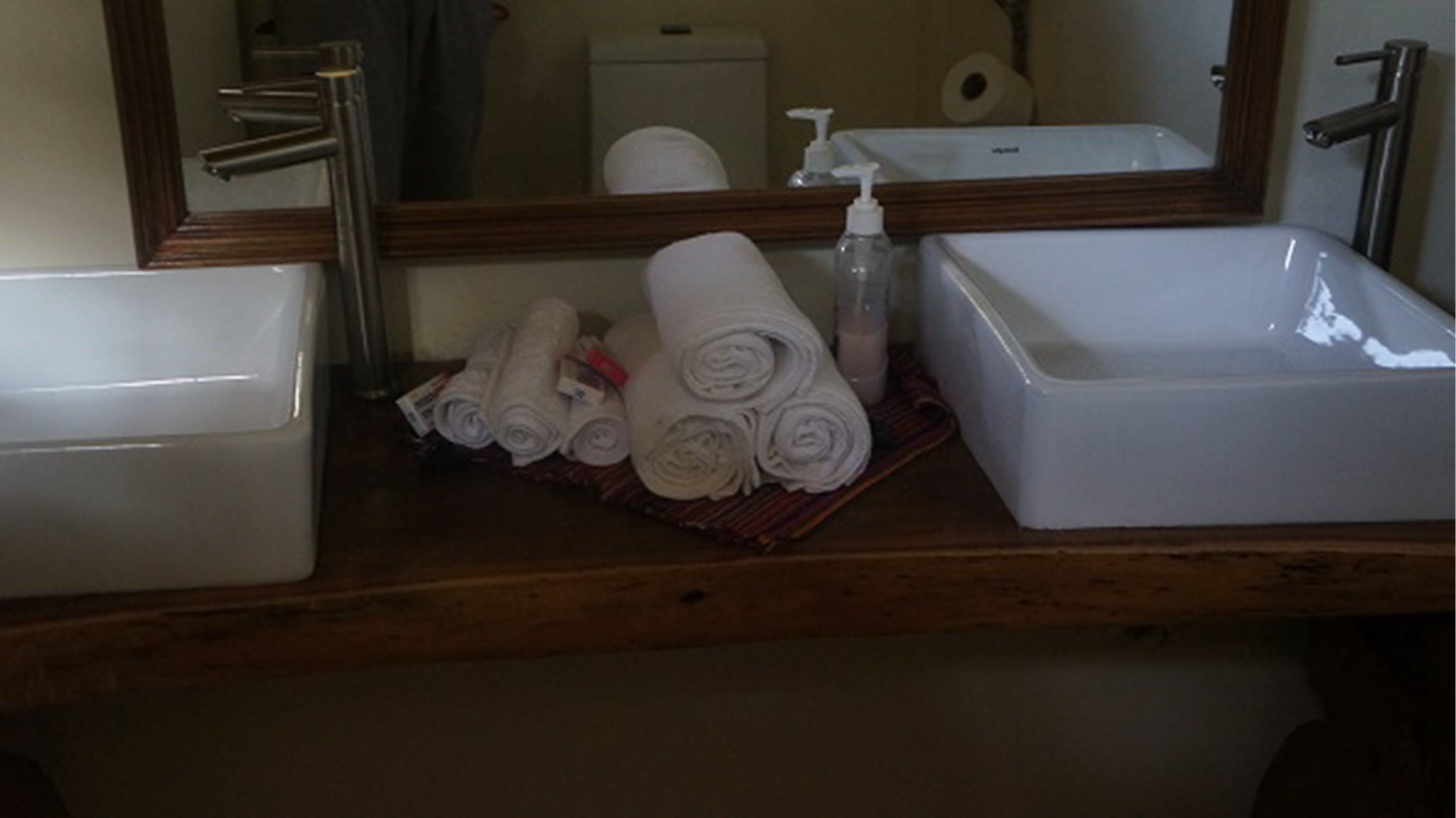 A bathroom with a wooden vanity, two sinks, a mirror, and towels.