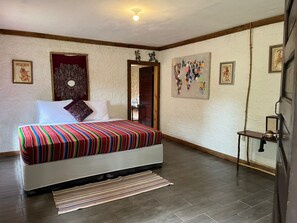 A bedroom with a bed, a wooden door, a small table, and a wall with framed artwork.