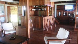 A wooden interior with a bar area, two white cushioned chairs, a wooden table with a smartphone, and a television on the wall. - Chez Paul Ambodiatafana (Ambodiatafana)